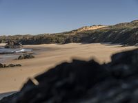 the view of a sandy beach with hills in the background and a surfboard in foreground