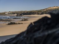 the view of a sandy beach with hills in the background and a surfboard in foreground