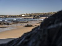 the view of a sandy beach with hills in the background and a surfboard in foreground