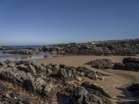 a rocky coast line near the ocean with boulders and rocks on the beach, looking out onto the water