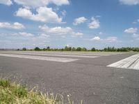 an empty runway in a city with grass on either side of the tarmac and a blue sky behind