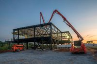 a picture of a building being built on a field near a forest in the background