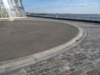 there is a black and white skateboarder riding in the empty place by the water