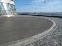 there is a black and white skateboarder riding in the empty place by the water