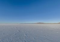 a large flat plain with many small footprints in the middle of it and mountains beyond