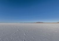 a large flat plain with many small footprints in the middle of it and mountains beyond