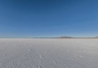 a large flat plain with many small footprints in the middle of it and mountains beyond