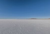 a large flat plain with many small footprints in the middle of it and mountains beyond