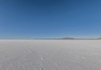 a large flat plain with many small footprints in the middle of it and mountains beyond