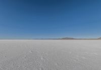 a large flat plain with many small footprints in the middle of it and mountains beyond