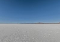 a large flat plain with many small footprints in the middle of it and mountains beyond