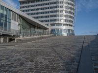 a modern building with a staircase that goes to it's top floor and is standing next to the steps on the cobblestone