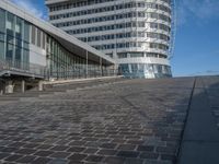 a modern building with a staircase that goes to it's top floor and is standing next to the steps on the cobblestone