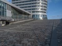 a modern building with a staircase that goes to it's top floor and is standing next to the steps on the cobblestone