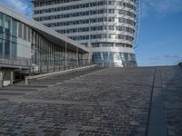 a modern building with a staircase that goes to it's top floor and is standing next to the steps on the cobblestone