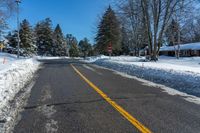 a street is covered with snow and trees along the road with a stop sign on the right side