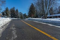 a street is covered with snow and trees along the road with a stop sign on the right side