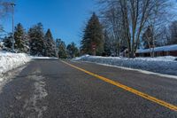 a street is covered with snow and trees along the road with a stop sign on the right side