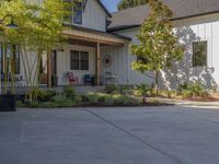 there is a house with a garage in the front of it and there are plants and trees growing on one side of the driveway