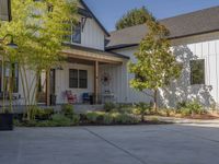 there is a house with a garage in the front of it and there are plants and trees growing on one side of the driveway