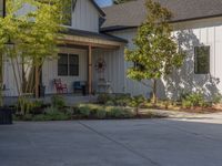 there is a house with a garage in the front of it and there are plants and trees growing on one side of the driveway