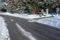 a paved road is lined with white snow and pine trees behind it, there's a sign in the middle of the street