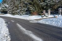 a paved road is lined with white snow and pine trees behind it, there's a sign in the middle of the street