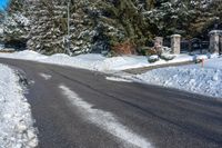 a paved road is lined with white snow and pine trees behind it, there's a sign in the middle of the street
