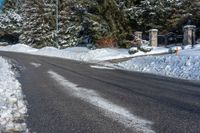 a paved road is lined with white snow and pine trees behind it, there's a sign in the middle of the street