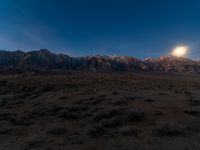 the moon is setting over a beautiful desert landscape with mountains in the background and plants