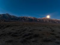 the moon is setting over a beautiful desert landscape with mountains in the background and plants