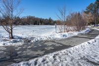 a paved area with trees, snow and ice all around it as well as sidewalk