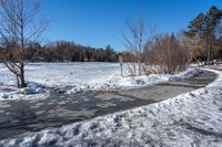 a paved area with trees, snow and ice all around it as well as sidewalk