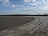 a man skateboards down the side of a wide walkway, by the water,