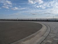 a man skateboards down the side of a wide walkway, by the water,