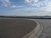 a man skateboards down the side of a wide walkway, by the water,