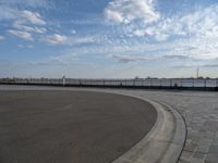 a man skateboards down the side of a wide walkway, by the water,