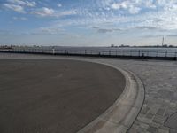 a man skateboards down the side of a wide walkway, by the water,