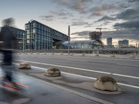 the buildings on the side of an urban road with cement boulders in front of them