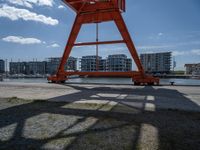 a crane that is sitting in the grass with buildings in the background, and clouds behind it