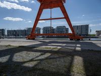 a crane that is sitting in the grass with buildings in the background, and clouds behind it