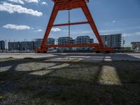 a crane that is sitting in the grass with buildings in the background, and clouds behind it