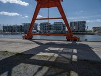 a crane that is sitting in the grass with buildings in the background, and clouds behind it