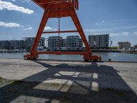 a crane that is sitting in the grass with buildings in the background, and clouds behind it