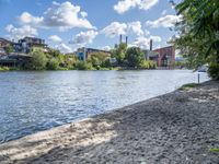 there is sand and water at this beach near buildings on the shore with lots of trees and bushes