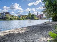 there is sand and water at this beach near buildings on the shore with lots of trees and bushes