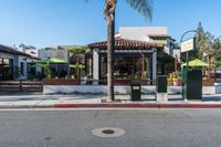 a small restaurant sits next to a street with palm trees and some benches next to it