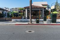 a small restaurant sits next to a street with palm trees and some benches next to it