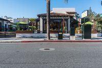 a small restaurant sits next to a street with palm trees and some benches next to it