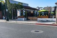 a city sidewalk with benches and tables at an intersection in a town setting at a business